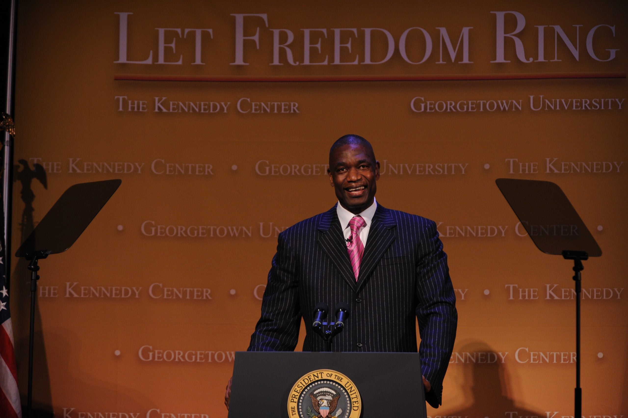 Dikembe Mutombo in front of a podium in a suit and tie