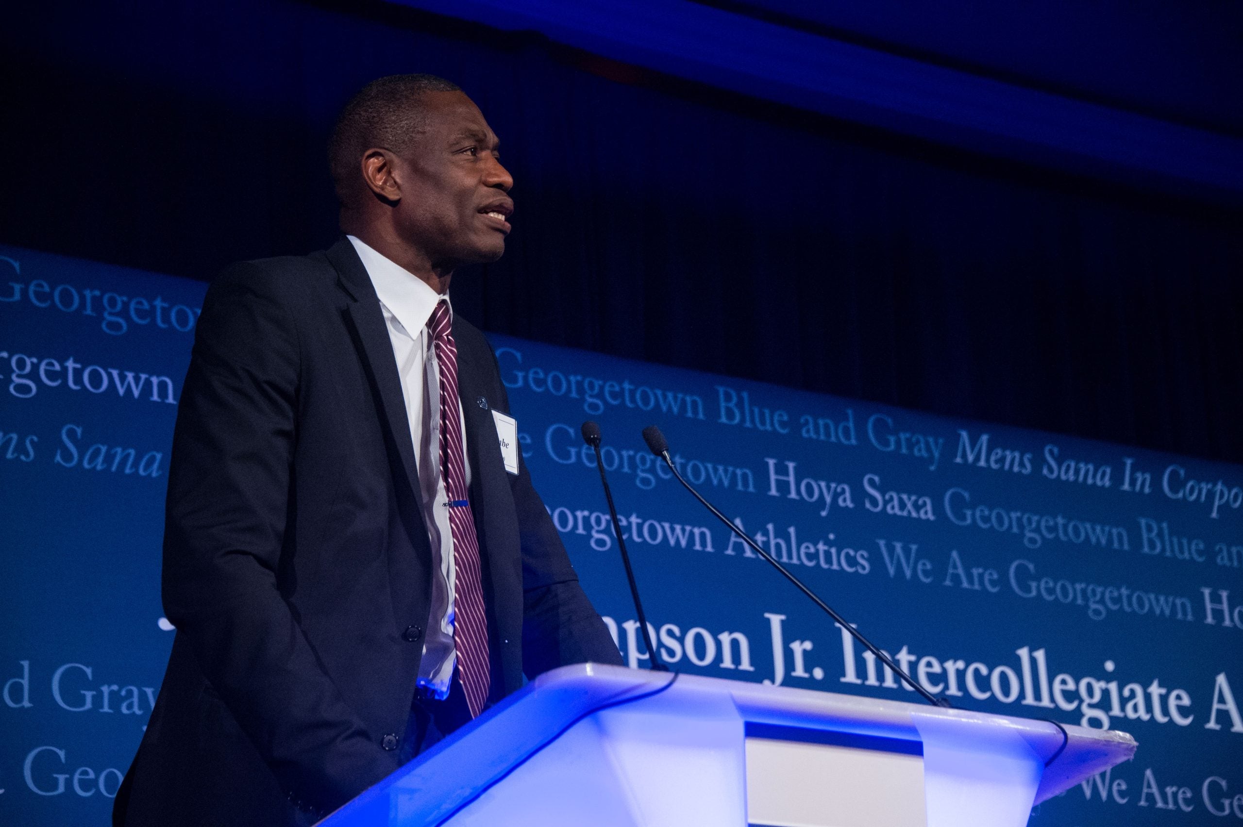 Dikembe Mutombo in a suit and tie speaks at a podium