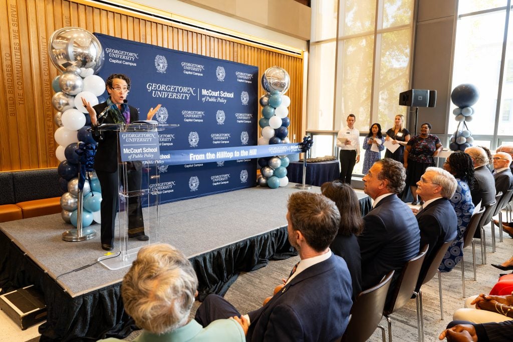 Maria Cancian speaking at a podium indoors with Georgetown logos behind her on a banner