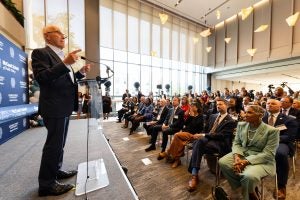 Frank McCourt in a suit talking to an audience in the atrium at 125 E