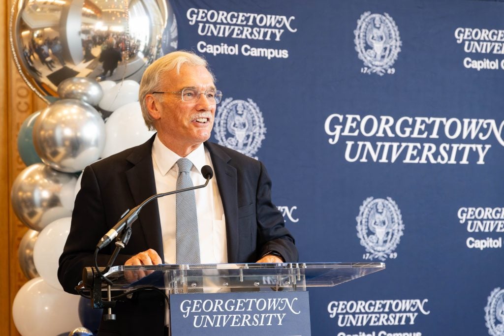 Provost Groves speaking at a podium with Georgetown logos behind him on a banner