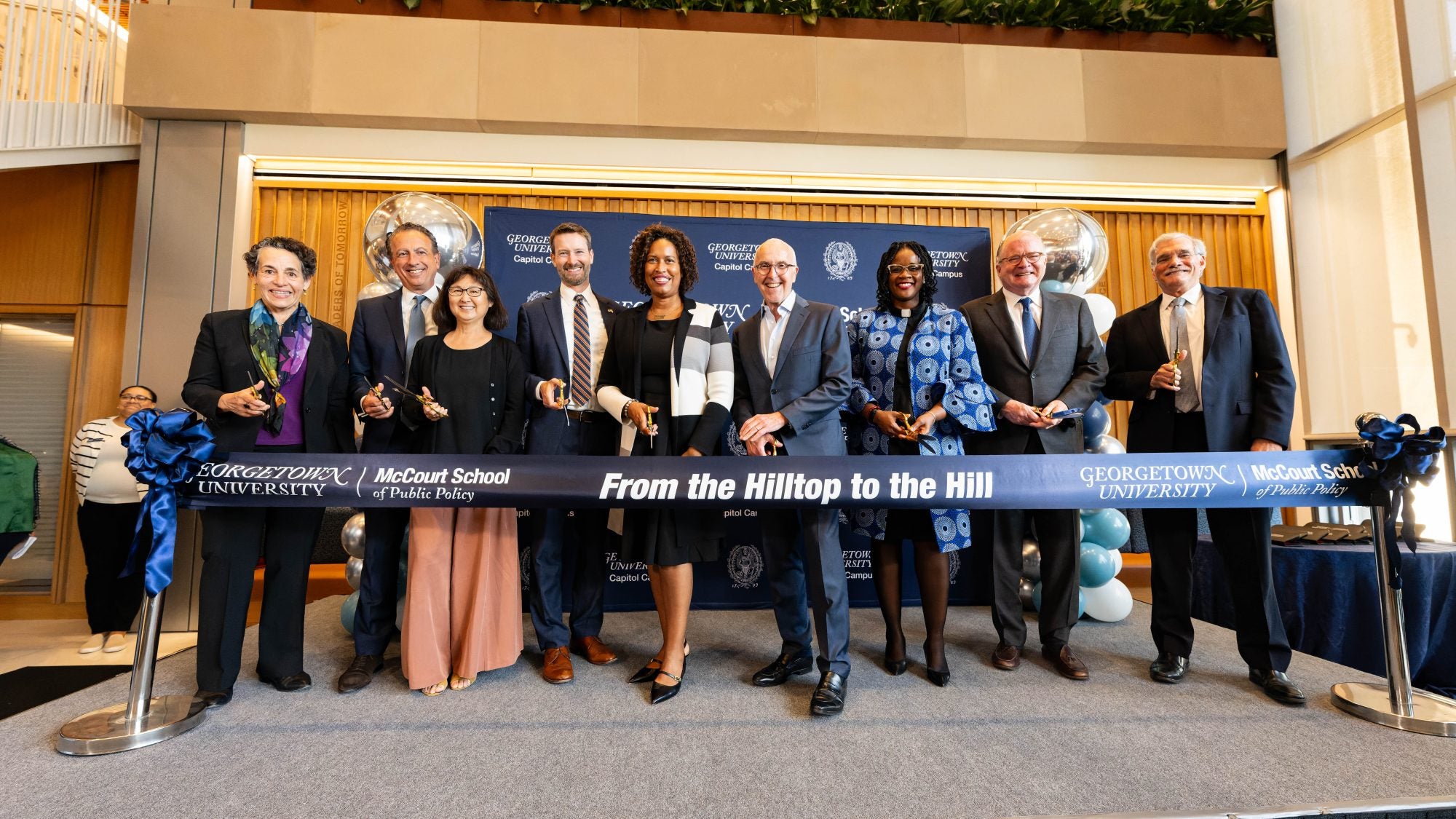 Nine people in doors with scissors about to cut a ribbon celebrating the opening of 125 E St.