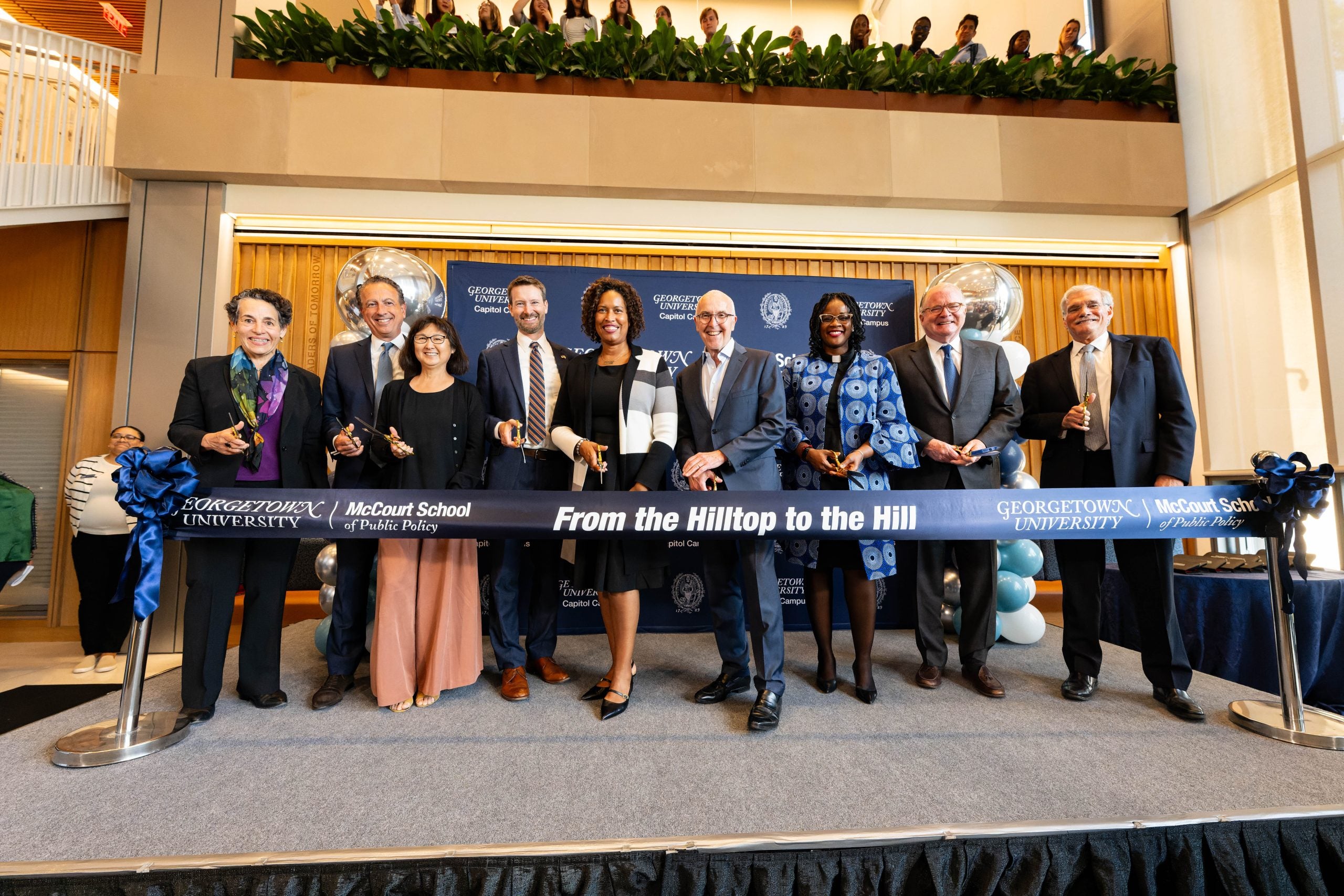 Nine people in doors with scissors about to cut a ribbon celebrating the opening of 125 E St.