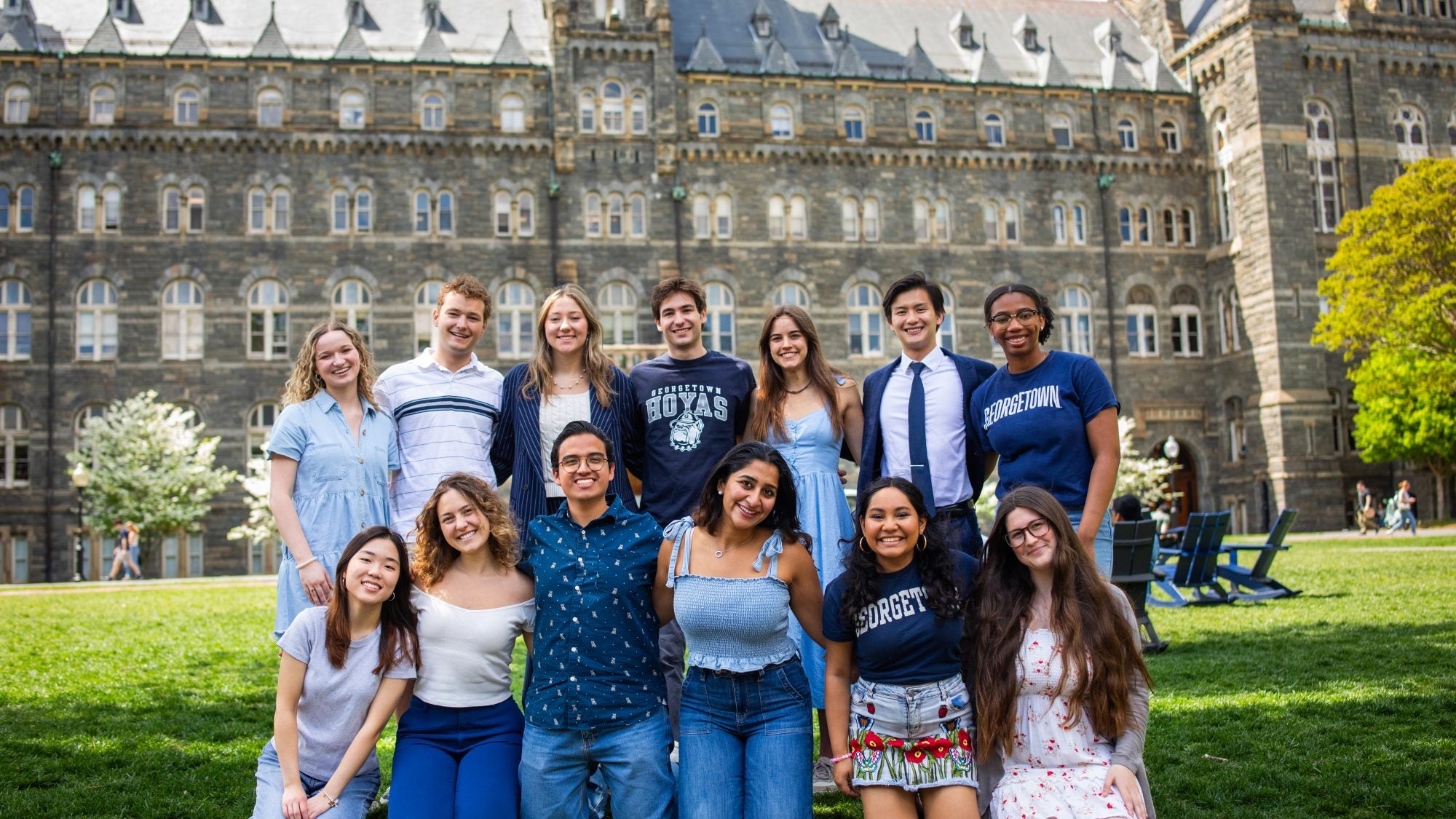 A group of students in GU gear in a group photo in front of Healy Hall on the lawn