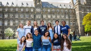 A group of students in GU gear in a group photo in front of Healy Hall on the lawn