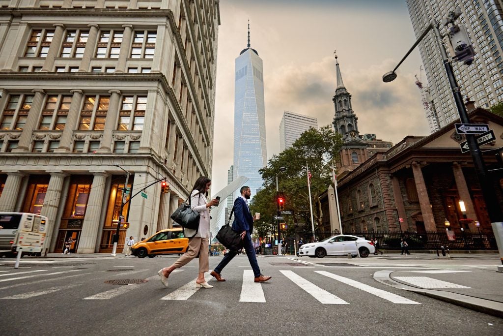 Two people crossing the street with the Freedom Tower in the background in New York City