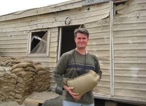 Gillen holding a sandbag outside next to a rundown building