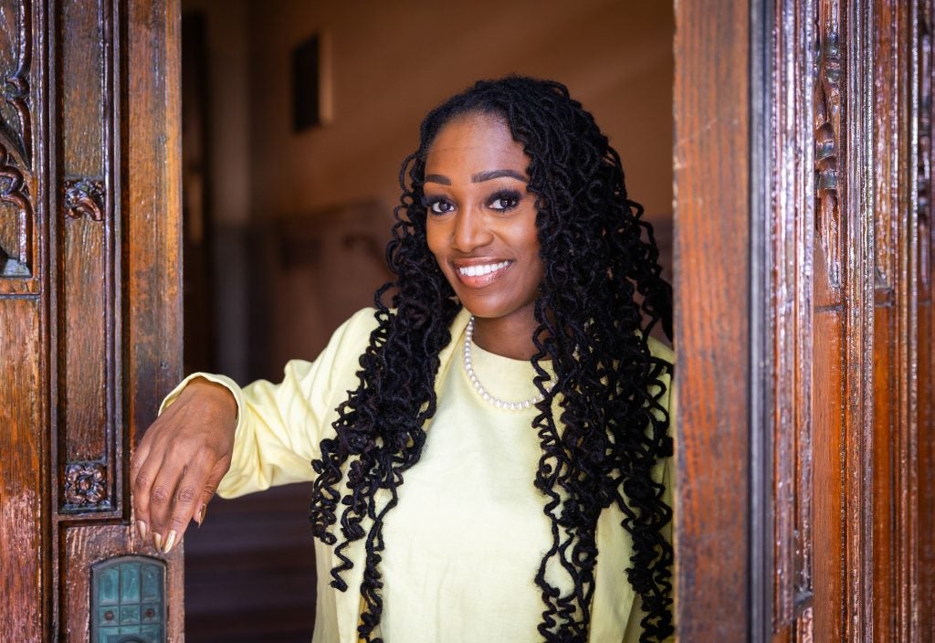 A woman with black curly hair smiles at the entrance to Healy Hall on Georgetown's campus.