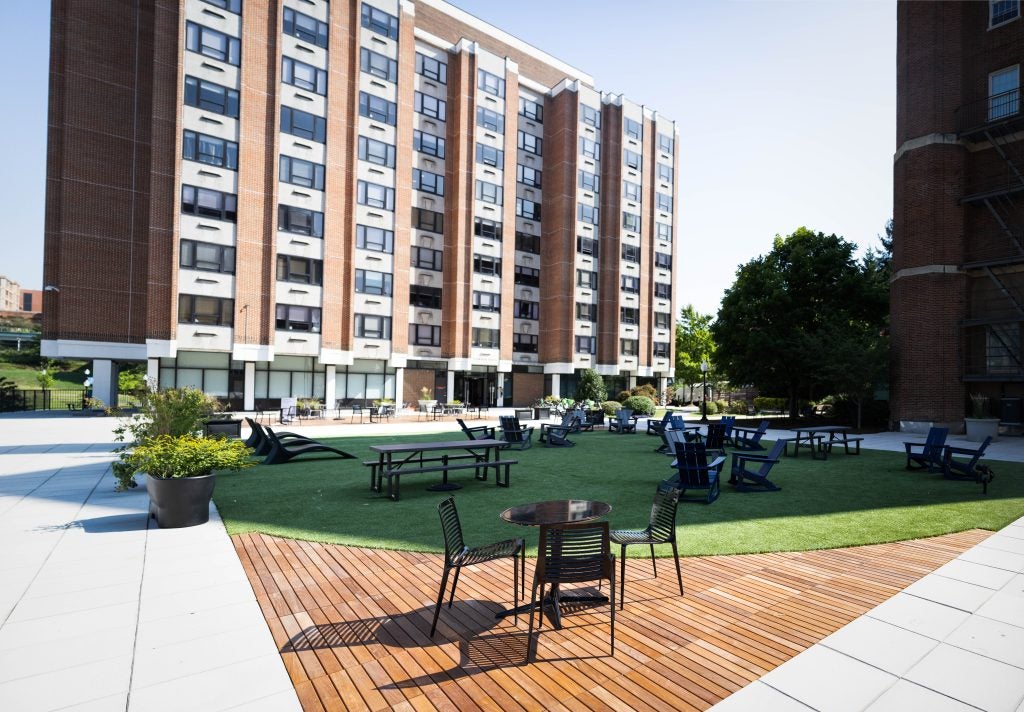 A residence building with a terrace in front. The terrace has a turf and table and chairs.