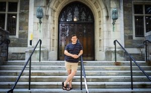 Troy outside of Copley Hall leaning on a railing on the steps