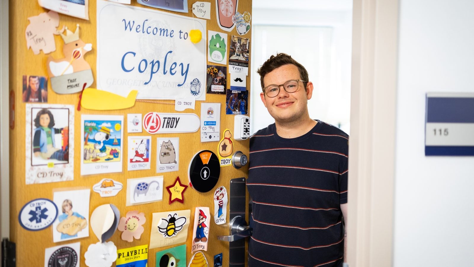 Troy in his office next to his door with many stickers welcoming people to Copley Hall