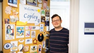 Troy in his office next to his door with many stickers welcoming people to Copley Hall