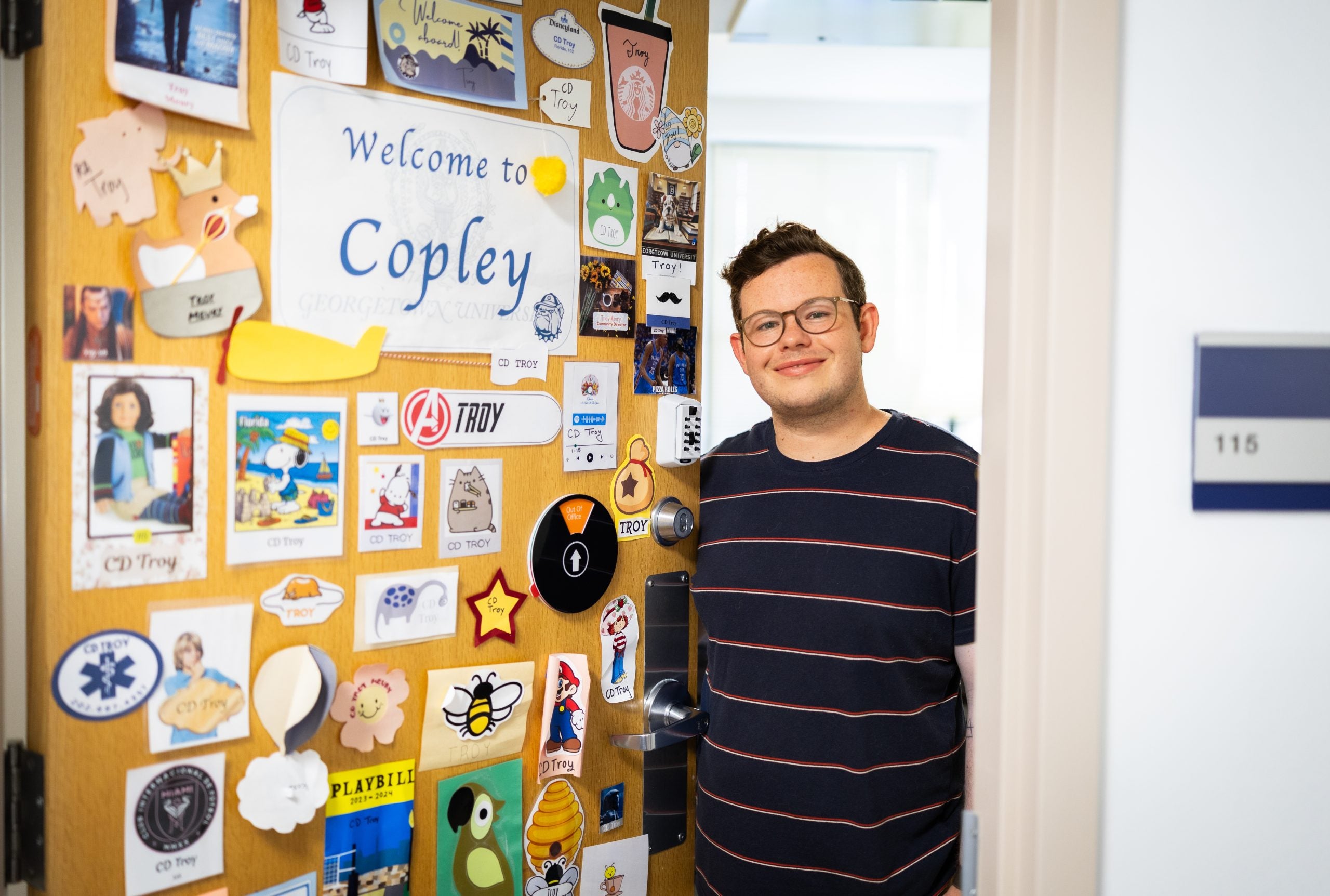 Troy in his office next to his door with many stickers welcoming people to Copley Hall