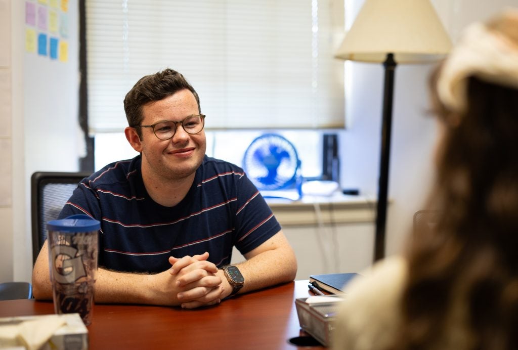 Troy speaking with a student and smiling at his desk