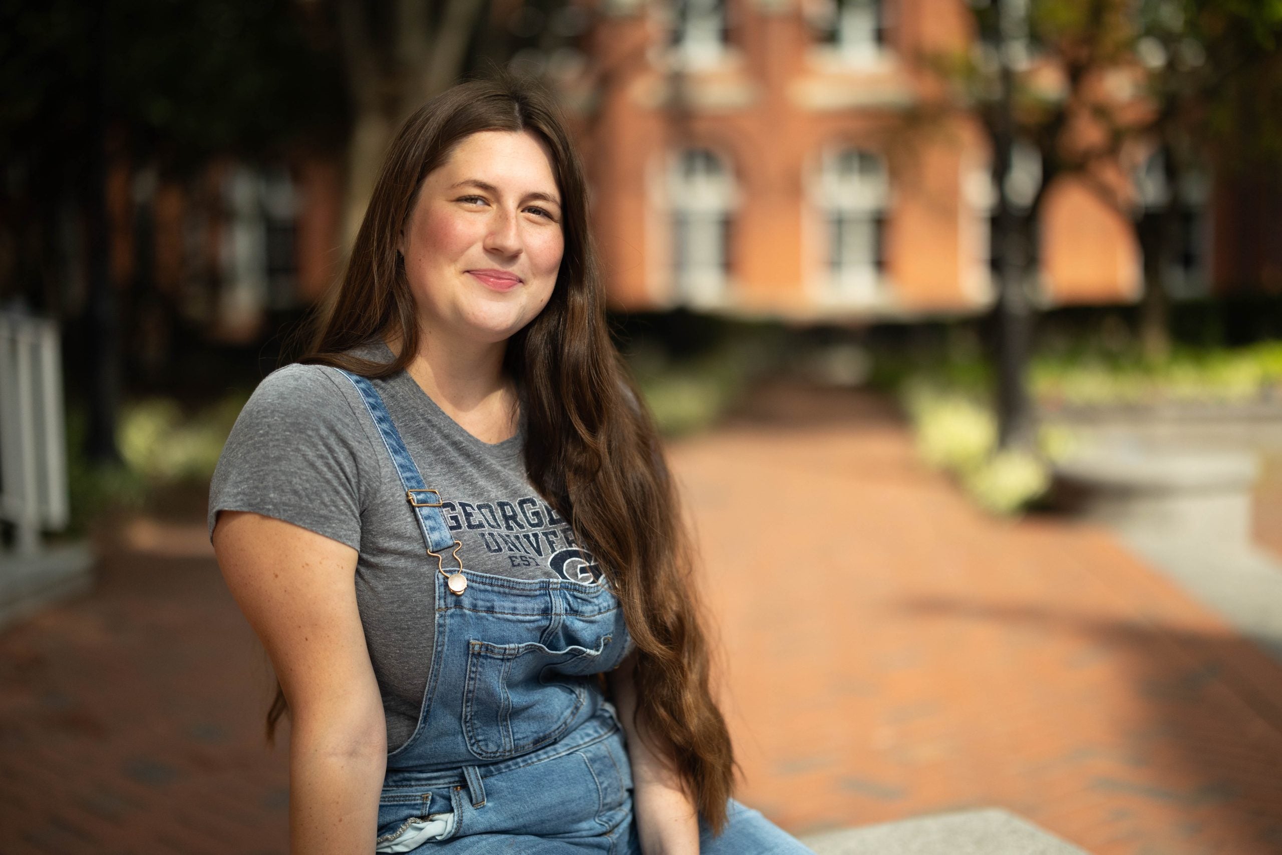 Sydney Carroll in a dark grey GU shirt and denim overalls on Dahlgren quad