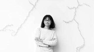 A black and white photo of a woman leaning against a wall wearing a white sweater.