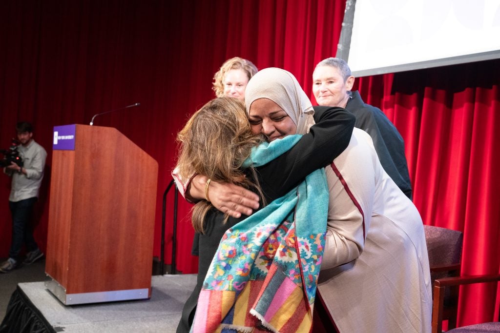 Two women hug each other just off a stage at New York University.