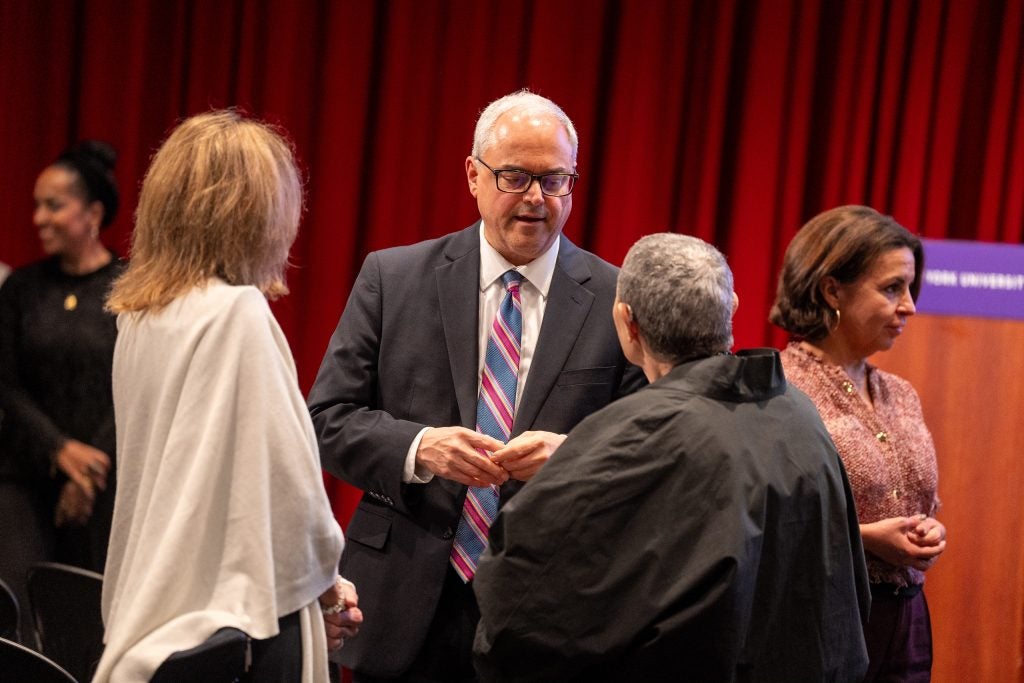 A group of people talk with one another in front of a red curtain.