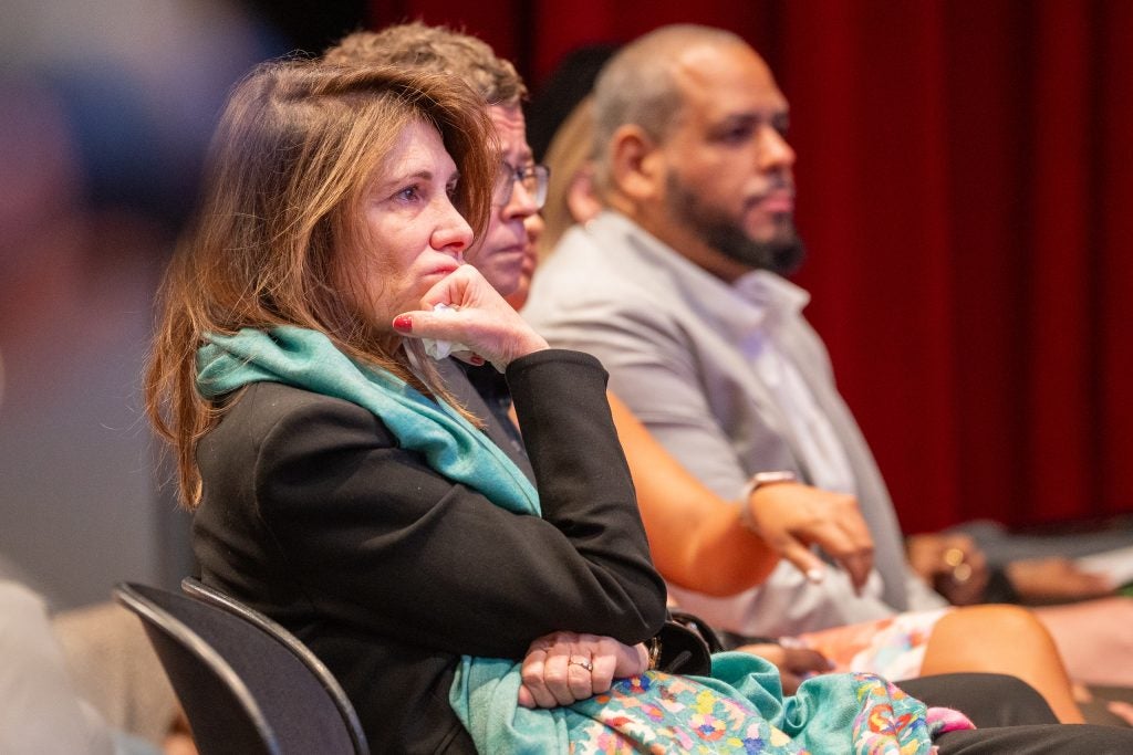 A woman seated in an audience rests her chin against her fist.