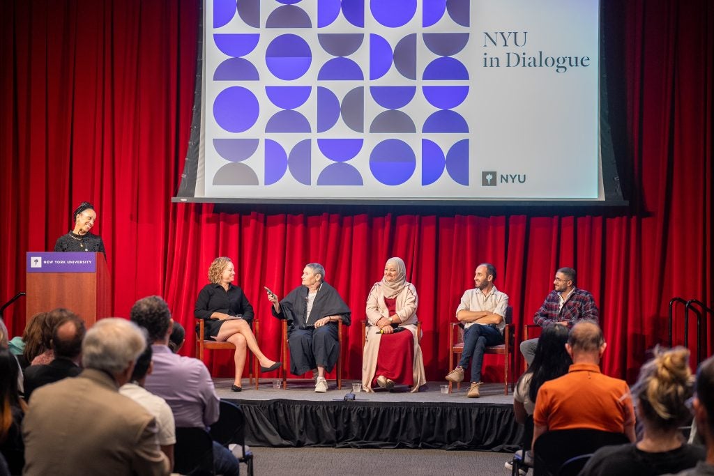 A group of panelists chat with one another on a stage at New York University.