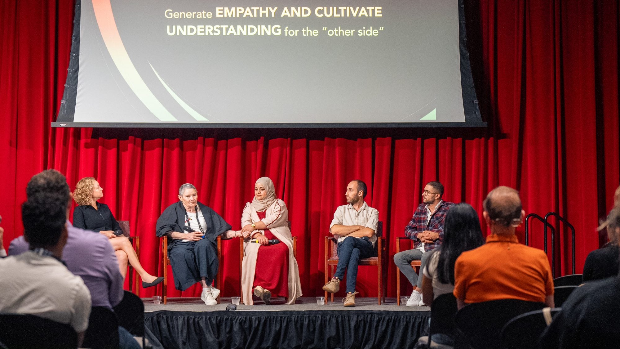 A group of panelists sit on a stage with a screen behind them.