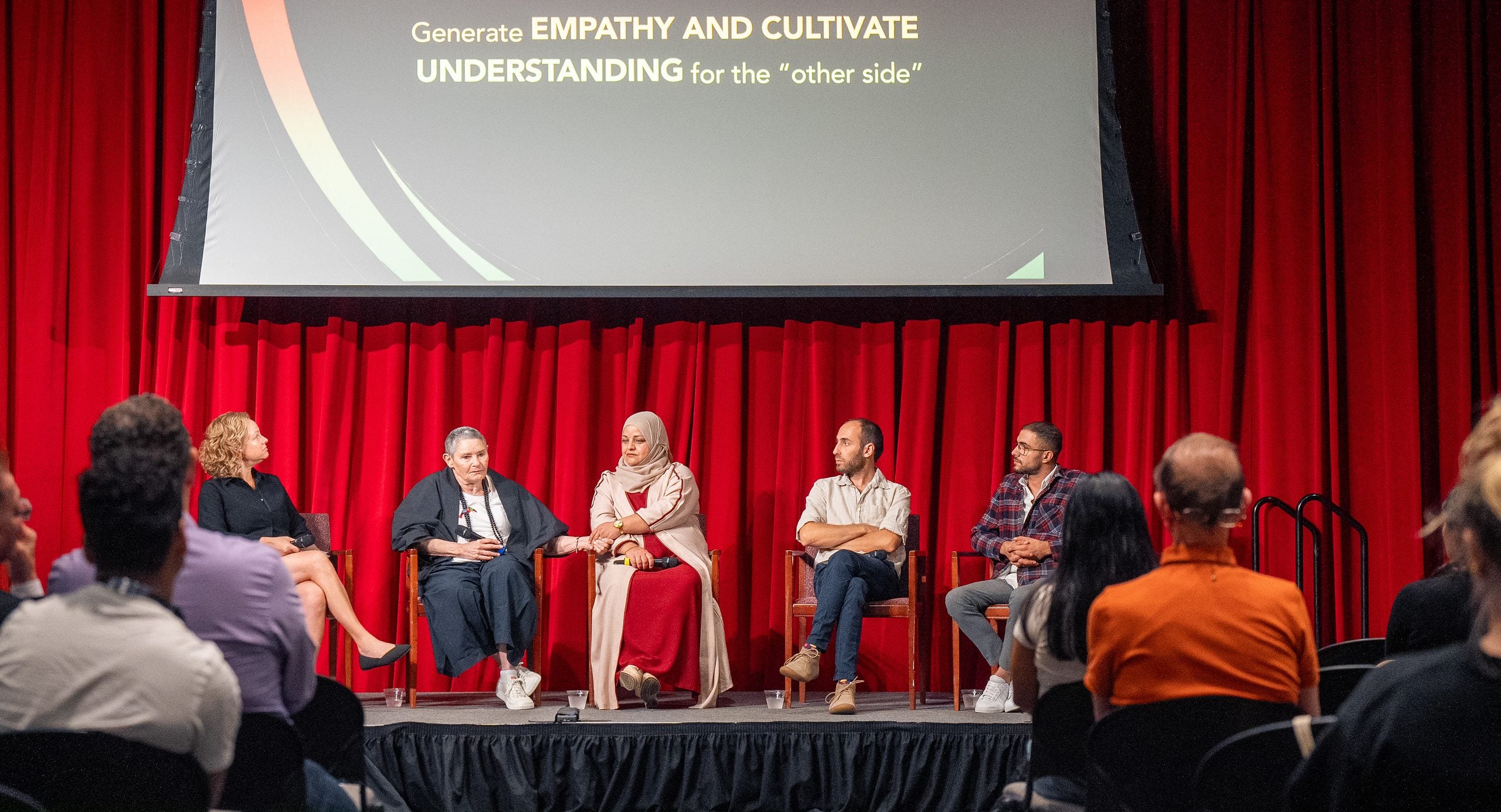 A group of panelists sit on a stage with a screen behind them.