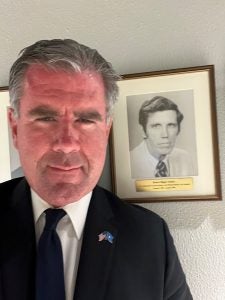 Selfie of Gillen in a suit next to a black and white photo of Amb. Oakley.