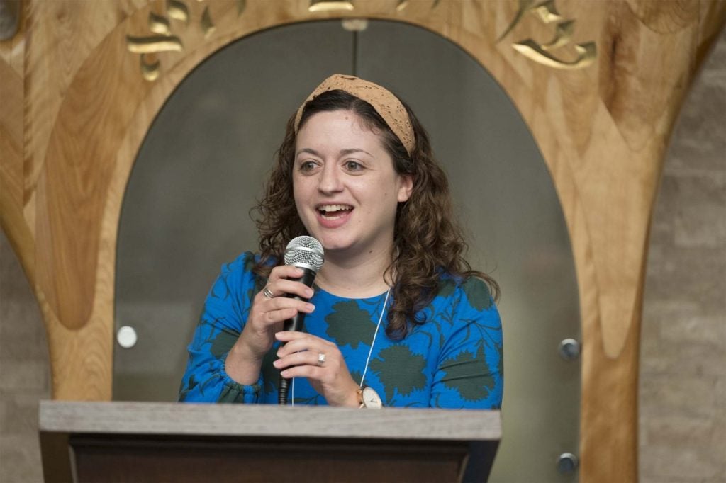 Rabbi Ilana Zietman in a blue dress talking behind a podium by the ark