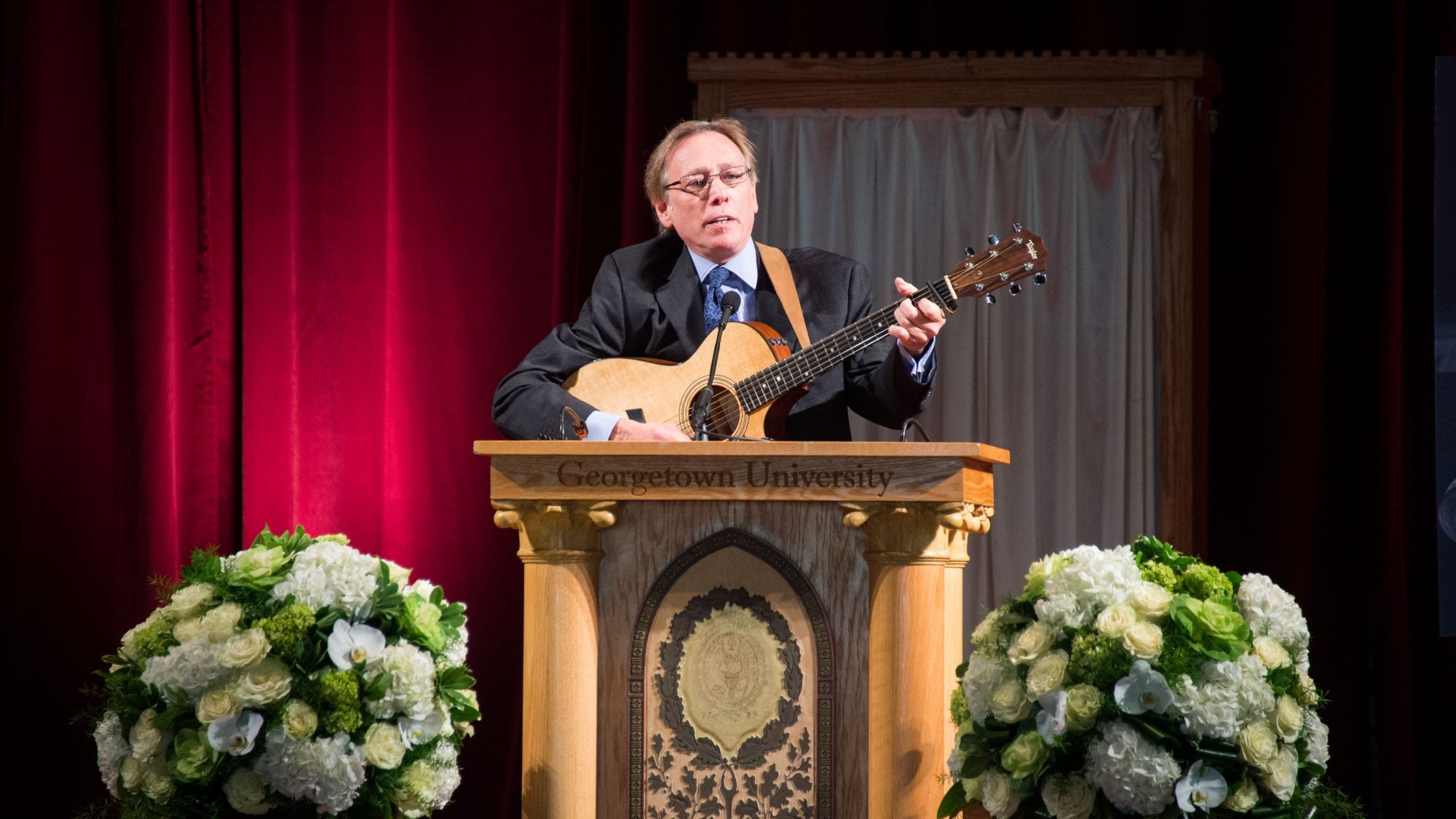 A man plays a guitar behind a podium on a stage.