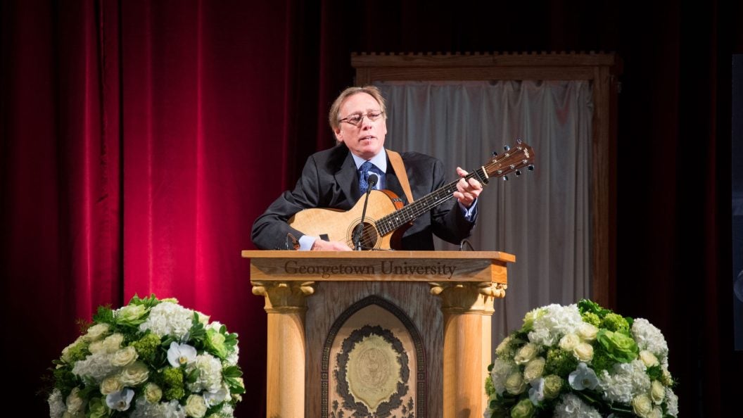 A man plays a guitar behind a podium on a stage.