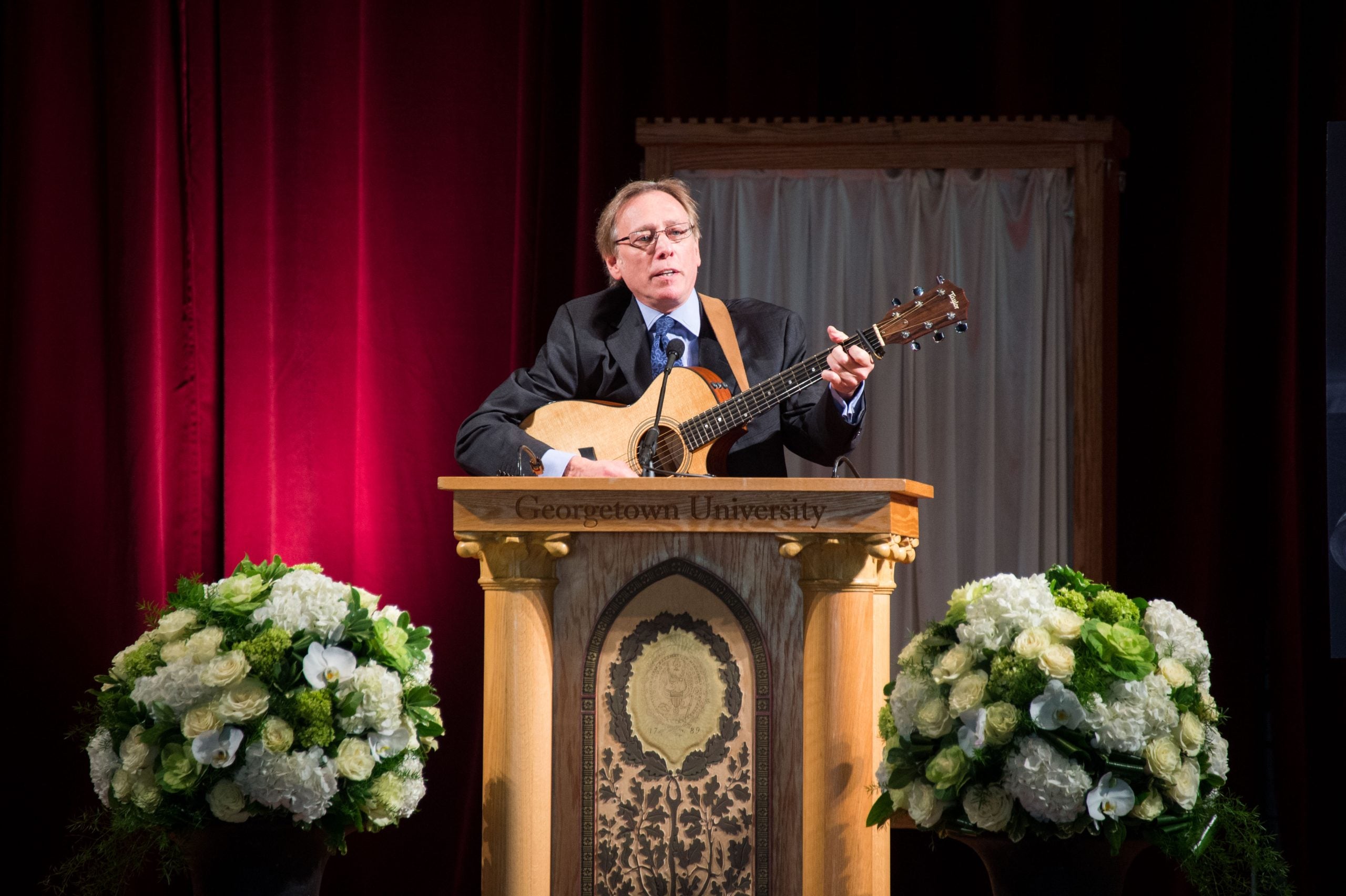 A man plays a guitar behind a podium on a stage.