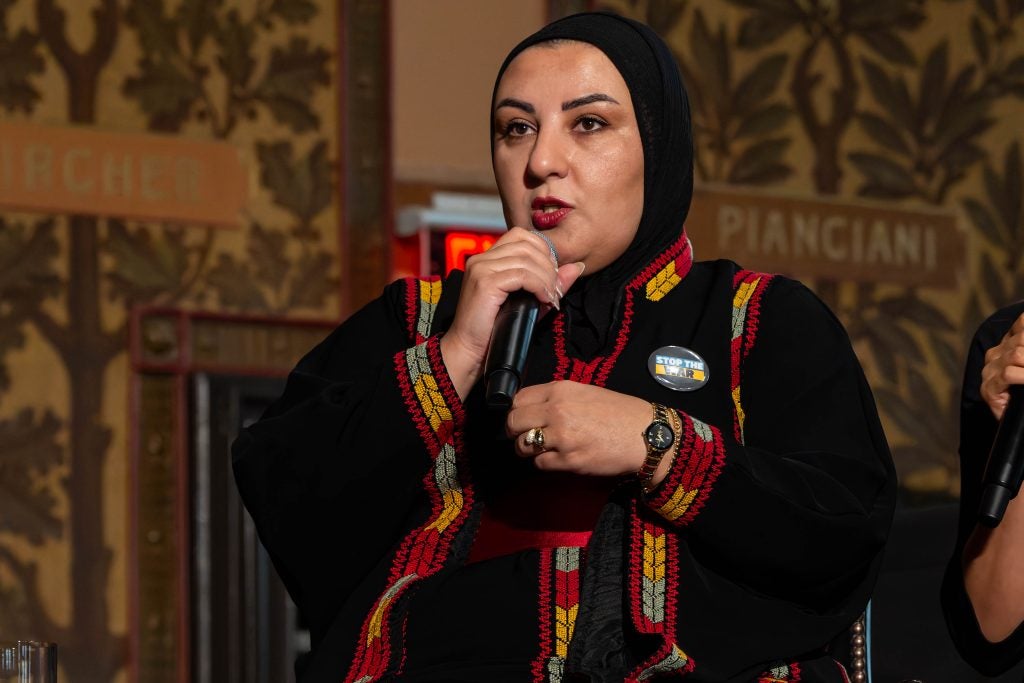 A woman in a hijab holds a microphone on a stage.