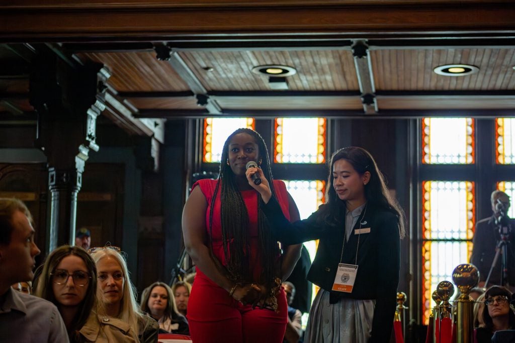 A student in a red dress asks a question in a mic.