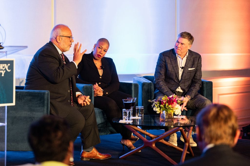 Three people speak on a stage in front of an audience.