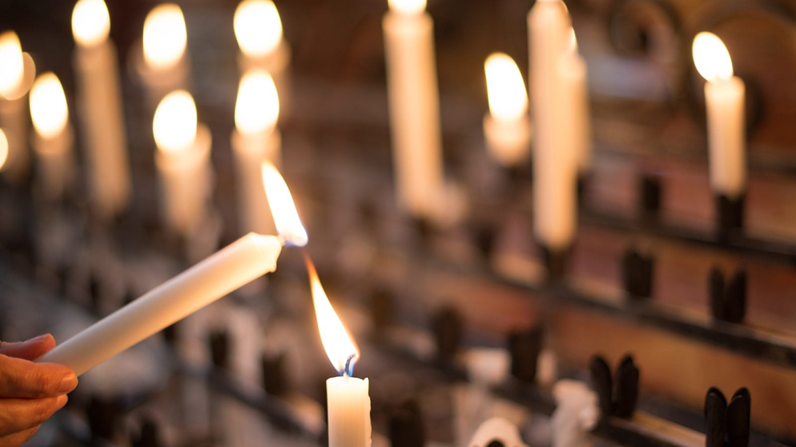 Woman lighting prayer candle aka offering, sacrificial or memorial candles lit in a church