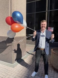 Patrick holding balloons and an American flag while in a suit