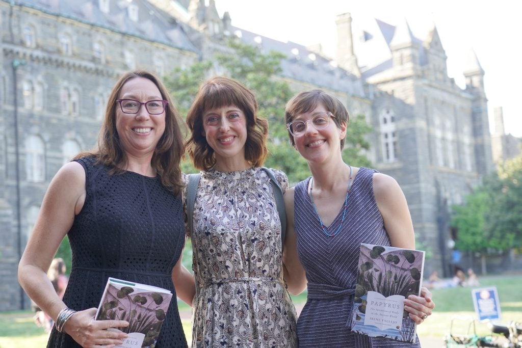 Three women pose in front of a stone building on Georgetown's campus.