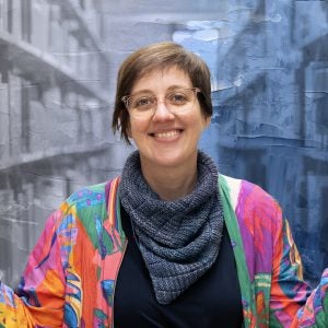 A woman in a colorful jacket smiles in front of a graphical image of shelves in a library.