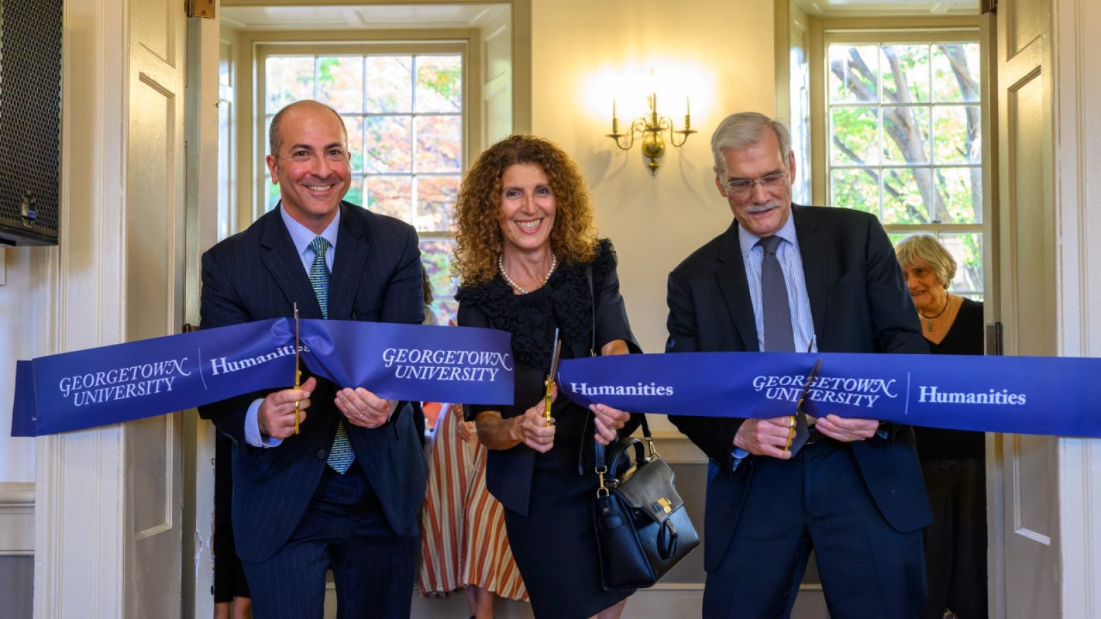 Two men and a woman cut a banner for the Georgetown Humanities Initiative in an academic building.