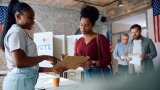 African American woman signing up to vote at polling place during US elections.