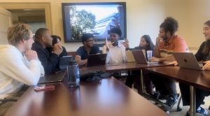 Justin Higgins speaking to other students at a conference table