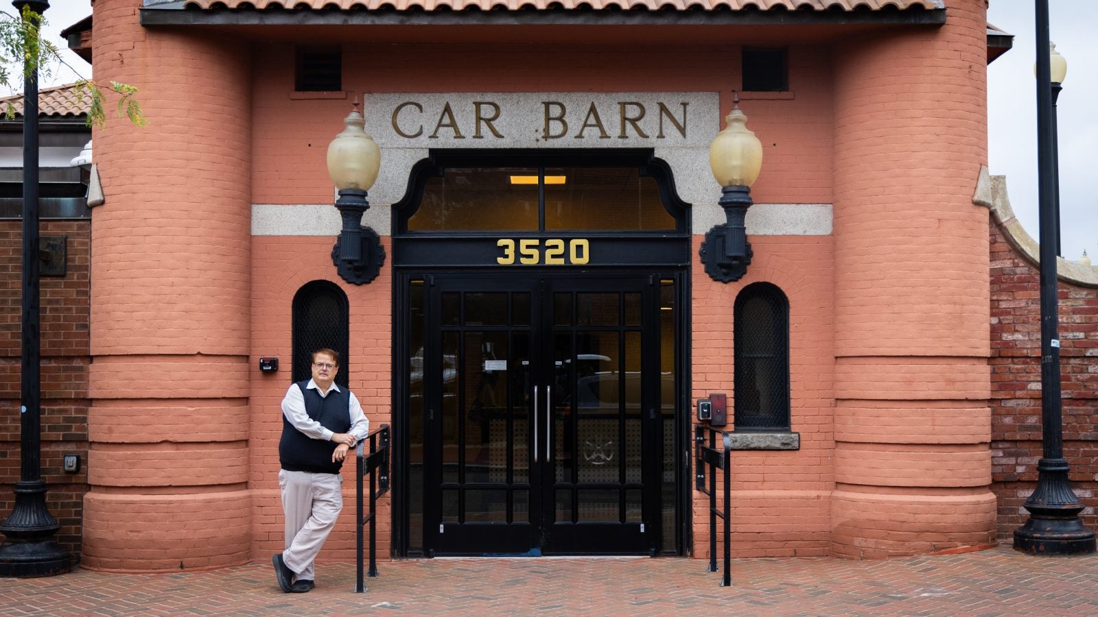 A man in a vest stands in front of a building that says &quot;Car Barn.&quot;