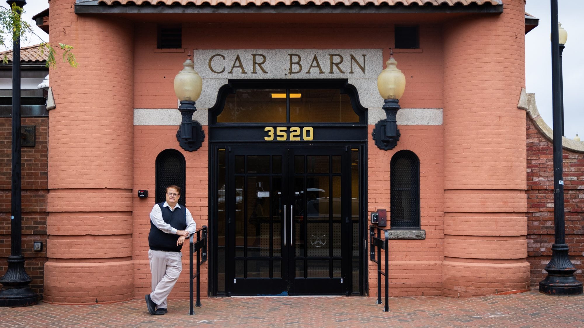 A man in a vest stands in front of a building that says &quot;Car Barn.&quot;