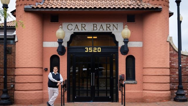 A man in a vest stands in front of a building that says &quot;Car Barn.&quot;