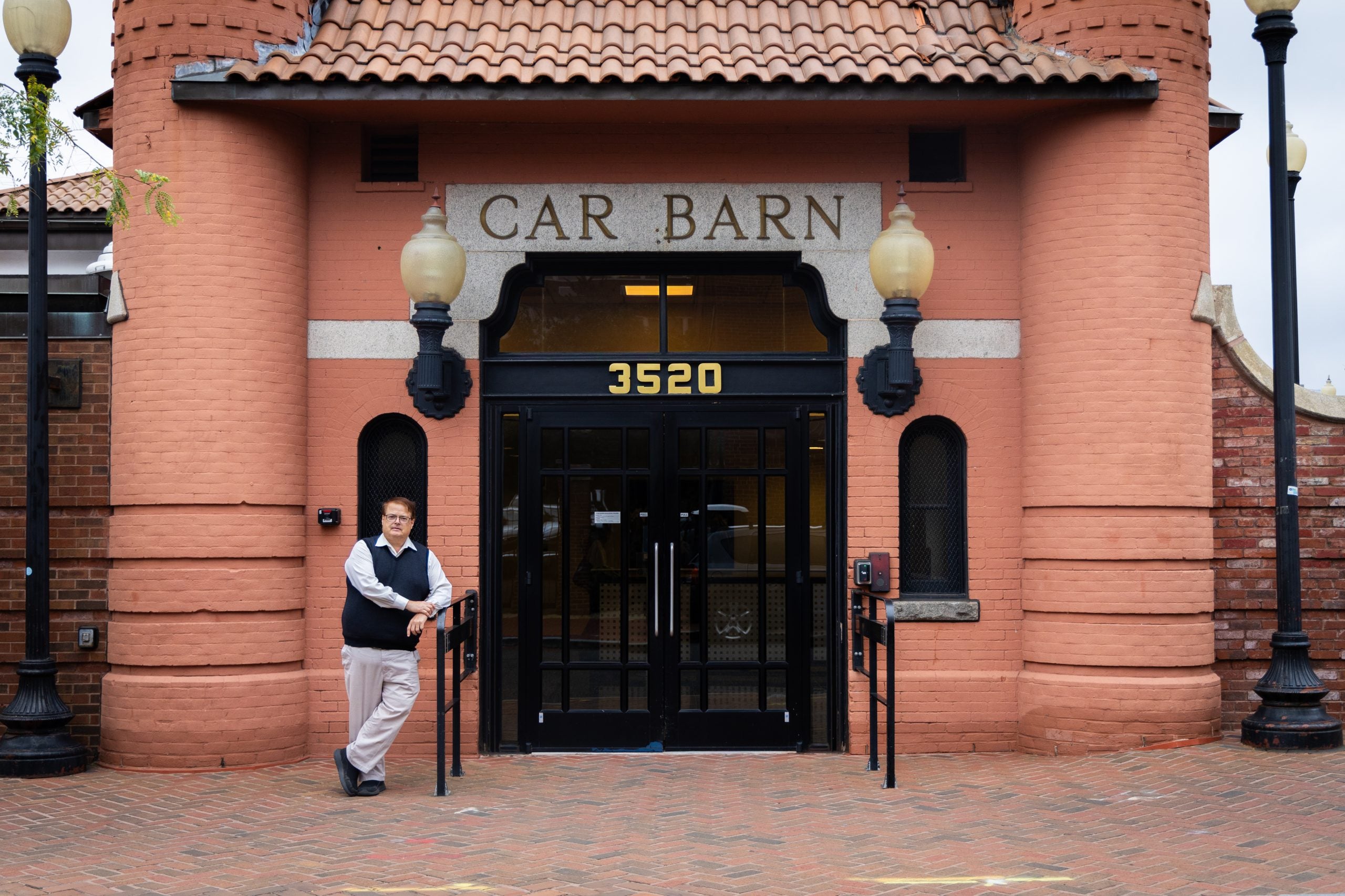 A man in a vest stands in front of a building that says "Car Barn."