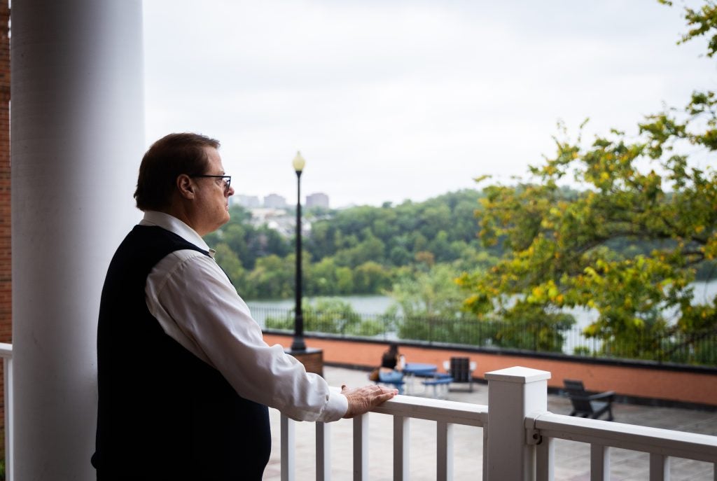 A man in a vest looks out over a patio onto the Potomac River.