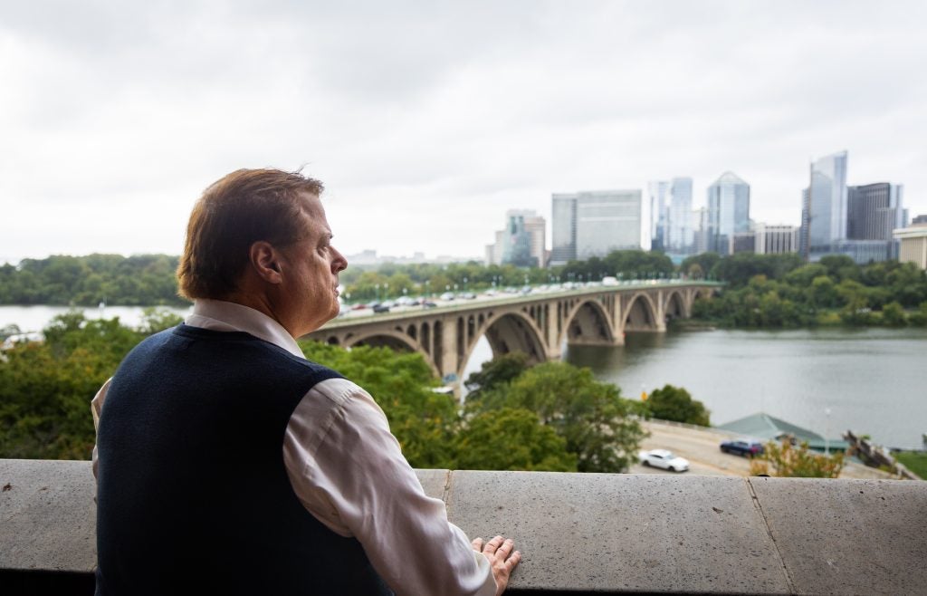 A man in a vest looks out over a bridge and the Potomac River.