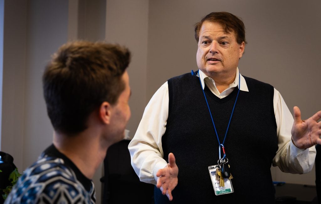 A white man in a vest speaks to a student.