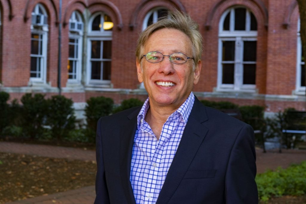 A man with glasses and a button-up shirt and suit smiles.