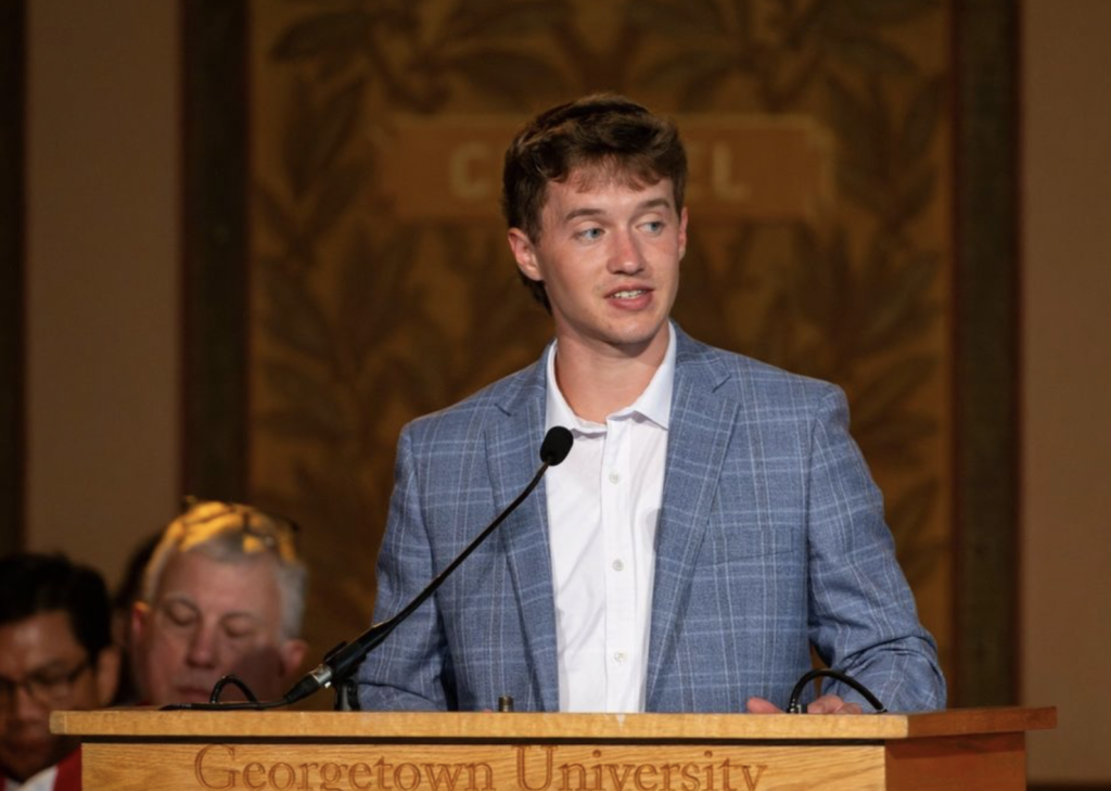 Luke in a gray blazer speaking at Mass in Gaston Hall